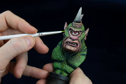 Person painting a small green creature figurine with a Ghost miniature paintbrush on a black background