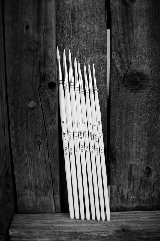Set of Ghost Miniature paint brushes leaning against a wooden surface