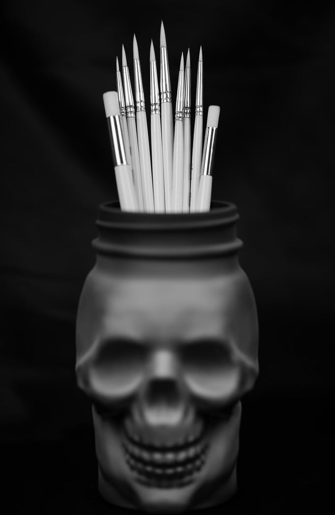 Skull-shaped container with Ghost paintbrushes on a black background
